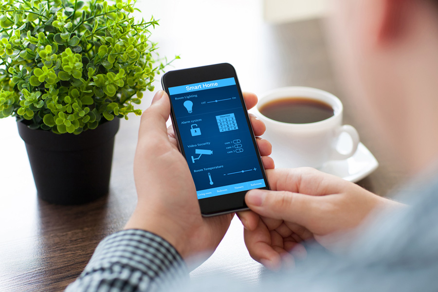 View of a man holding a phone with a smart home screen on a desk.